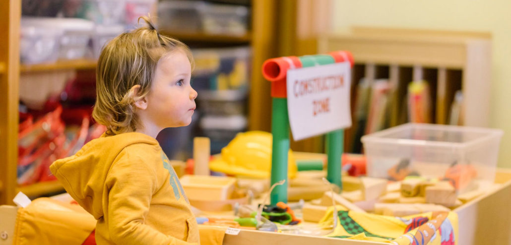 A toddler is learning to create child art indoors while their yellow-clad face beams with joy.