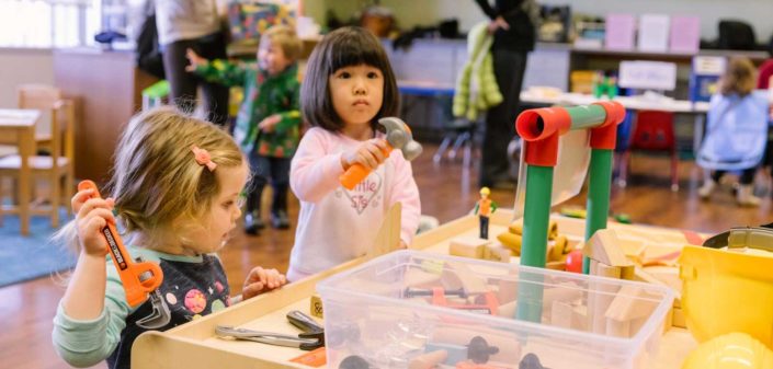 A person and a person are happily creating art together at a preschool table filled with plastic toys.