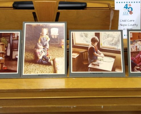 A picture frame filled with art hangs on the wall of a library filled with furniture in an indoor setting of 4th Child Care Napa County in 1979.