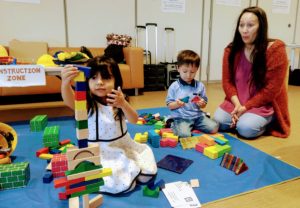 A kindergarten-aged person and person are happily playing with LEGO and a toy while learning and creating child art in an indoor family school setting.