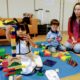 A kindergarten-aged person and person are happily playing with LEGO and a toy while learning and creating child art in an indoor family school setting.