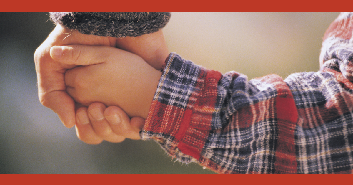 A newborn baby's hand grasps a plaid tartan fabric with their thumb and finger nails exposed.
