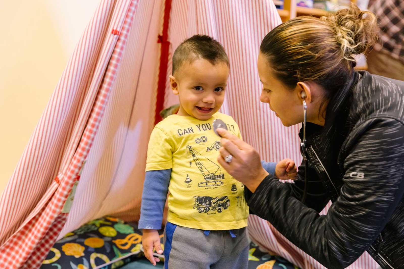 A young woman plays doctor with her toddler son.