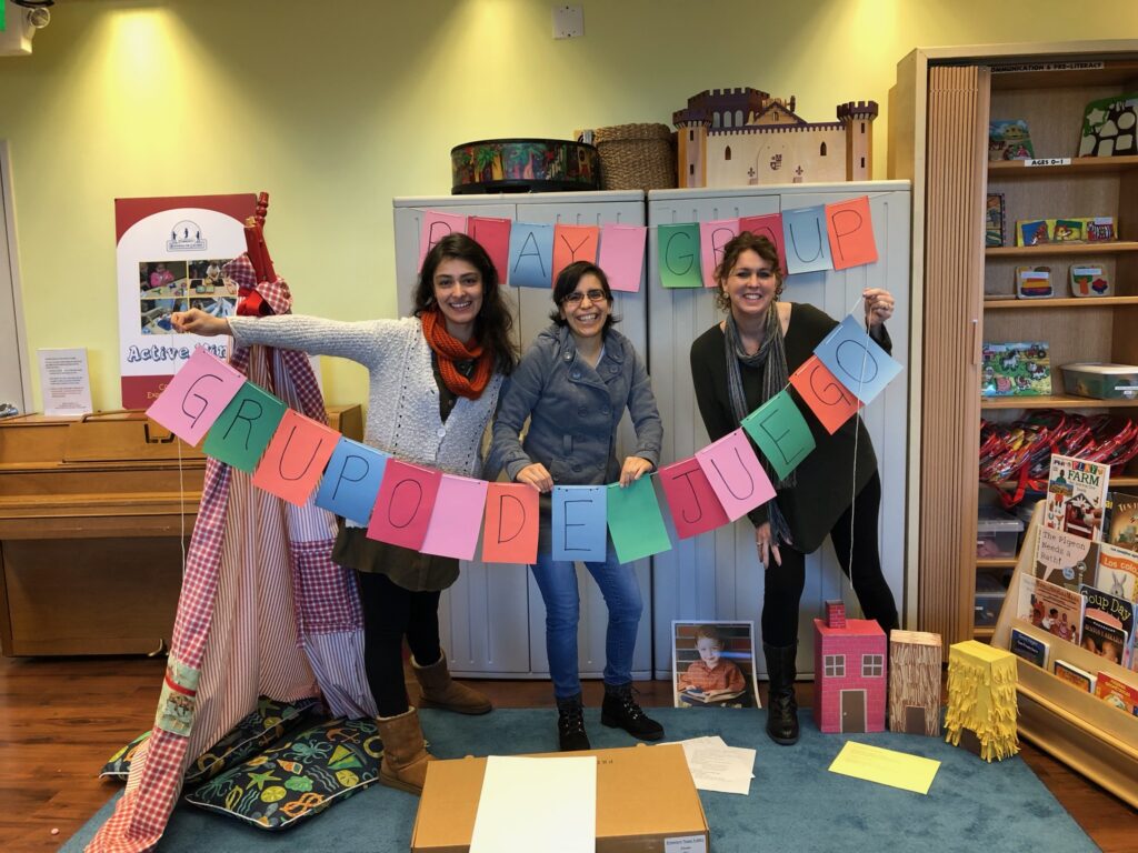 A family of three stands in a library, smiling as they browse the shelves of books and furniture.